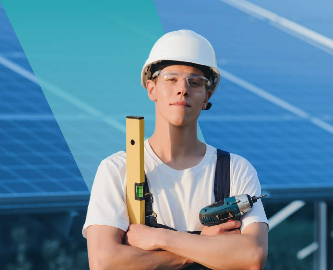 Confident solar technician in safety helmet holding spirit level and electric drill, standing in front of solavita solar panels