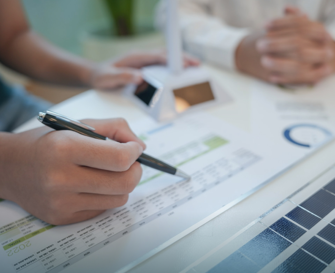 Close-up of hands analyzing solar panel investment plan with charts, calculator, and financial data.
