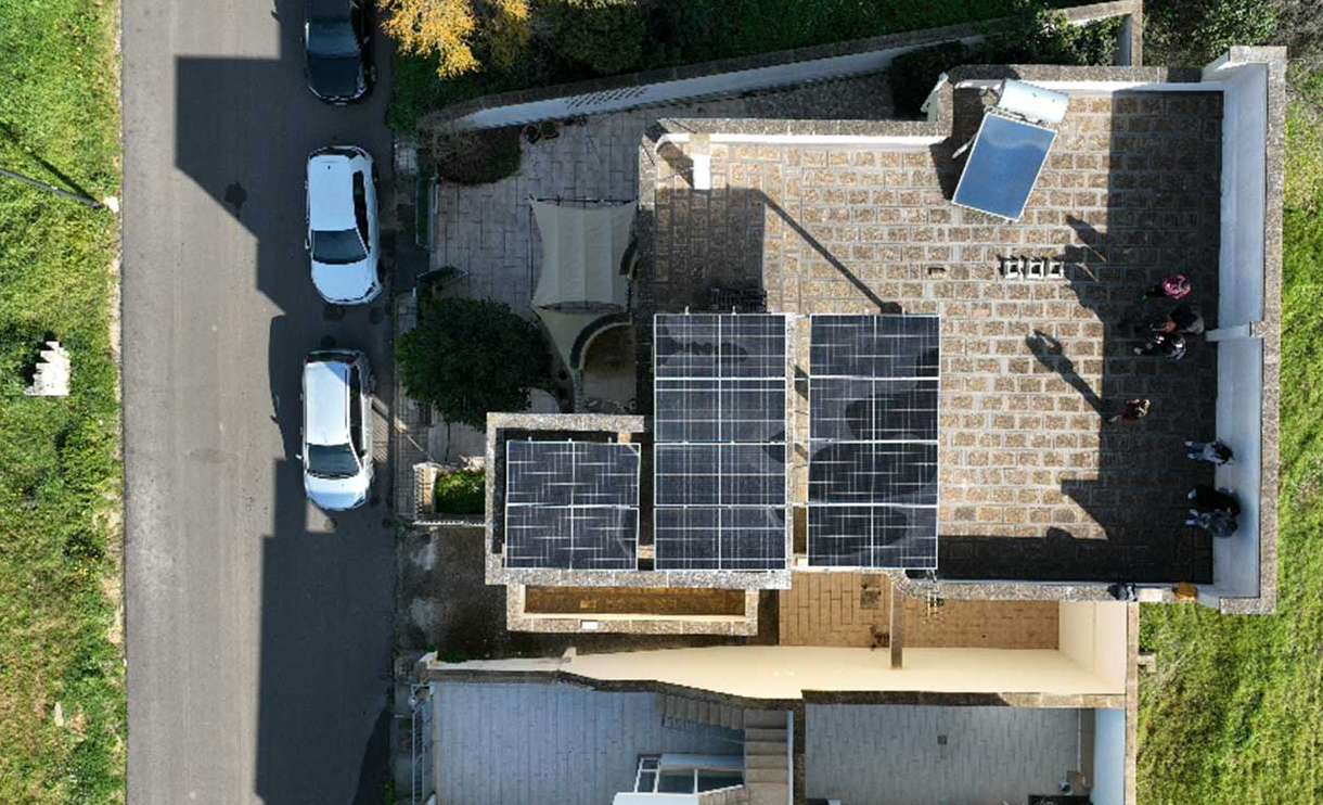 Top-down view of a residential flat roof equipped with a modular solar panel system and a solar water heater, with visible maintenance personnel standing on the rooftop.