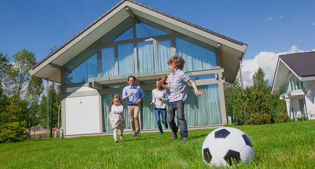 Happy family playing on green lawn in front of a modern home, representing clean and sustainable living with solar energy