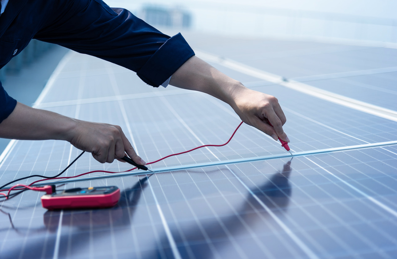 Technician testing a solar panel with a multimeter, inspecting the solar cells