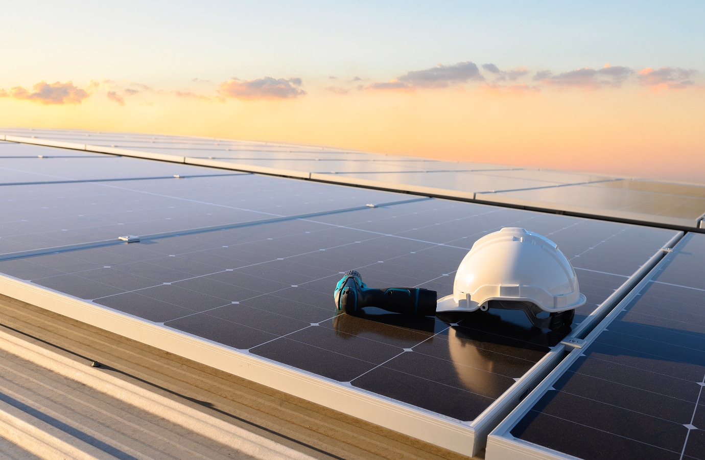 Solar panel on a rooftop with a helmet and tool resting on it, set against a sunset sky.